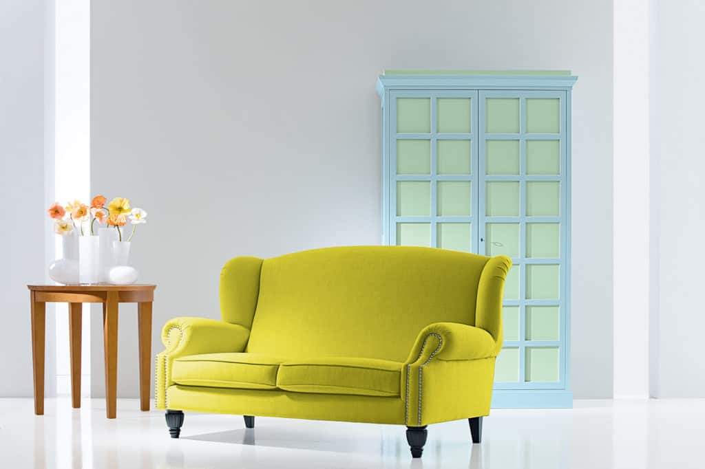 Massivholz-Kleiderschrank aus zweifarbig lasierter Pinie, Modell 5385, hellblau mit hellgrünen Türfüllungen und klassischem Design. Runder Beistelltisch aus honigfarbener Pinie, Modell 6048/68, Höhe 68 cm, Durchmesser 68 cm, aus Massivholz gefertigt. Sofa Bergerona mit elegantem Design und komfortabler Polsterung für stilvolle Wohnräume